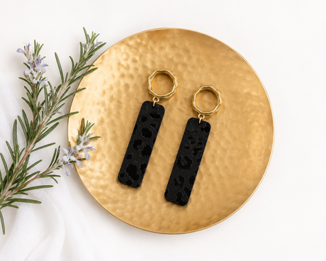 Black Leopard Dangle Earrings on a matte gold plate with a sprig of rosemary on the side